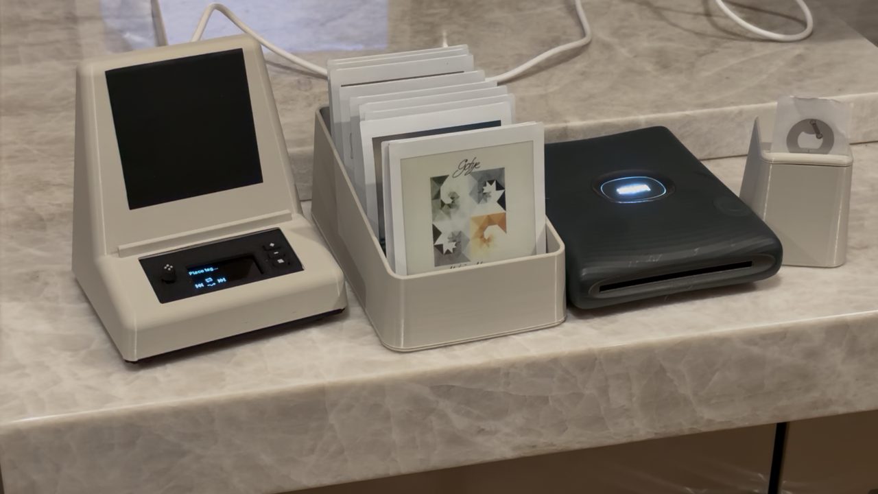 A Spotifactory on a counter, next to a crate of album photos, an Instax Square Link printer and a holder of NFC stickers
